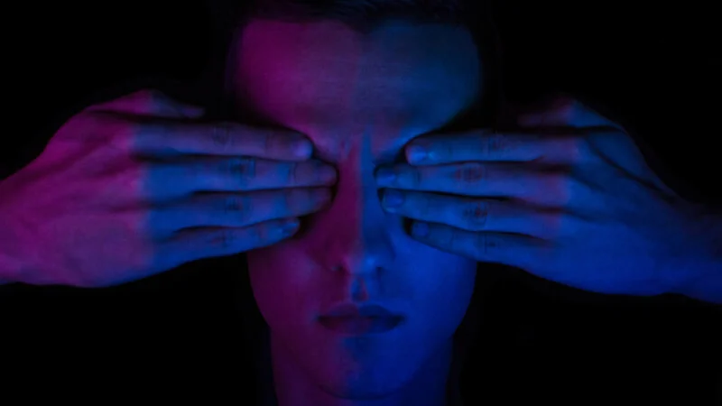 A person in the dark with hands covering their eyes.