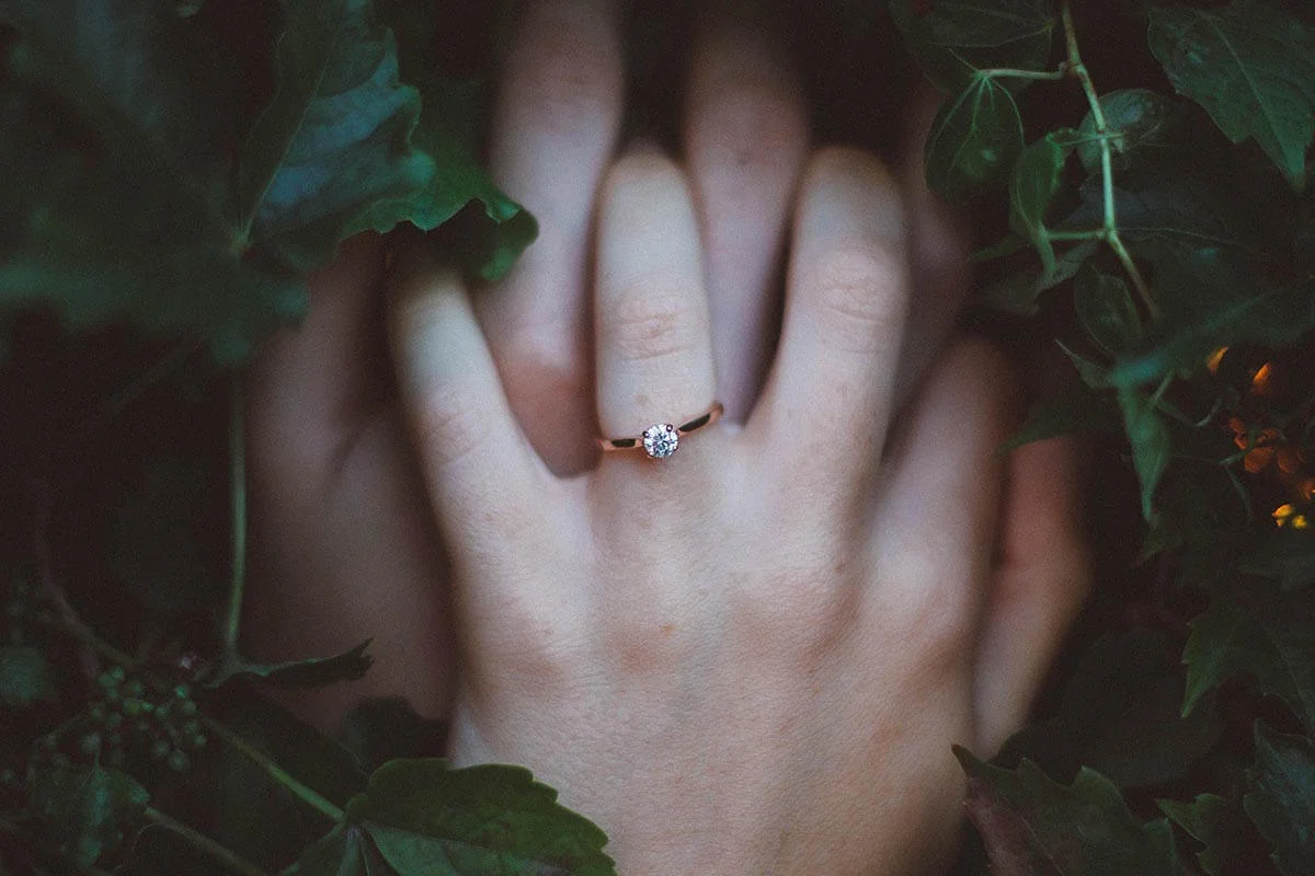 Two hands with wedding rings clasping each other in a bed of ivy.