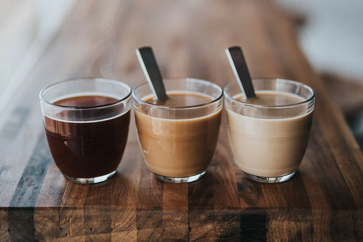 Three small clear glasses set in a row with dark coffee, medium brown coffee, and light coffee