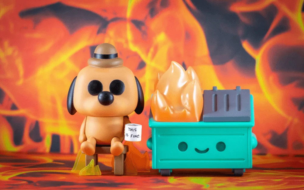 Toy dog sitting in front of a fire and dumpster fire with a mug that says this is fine.